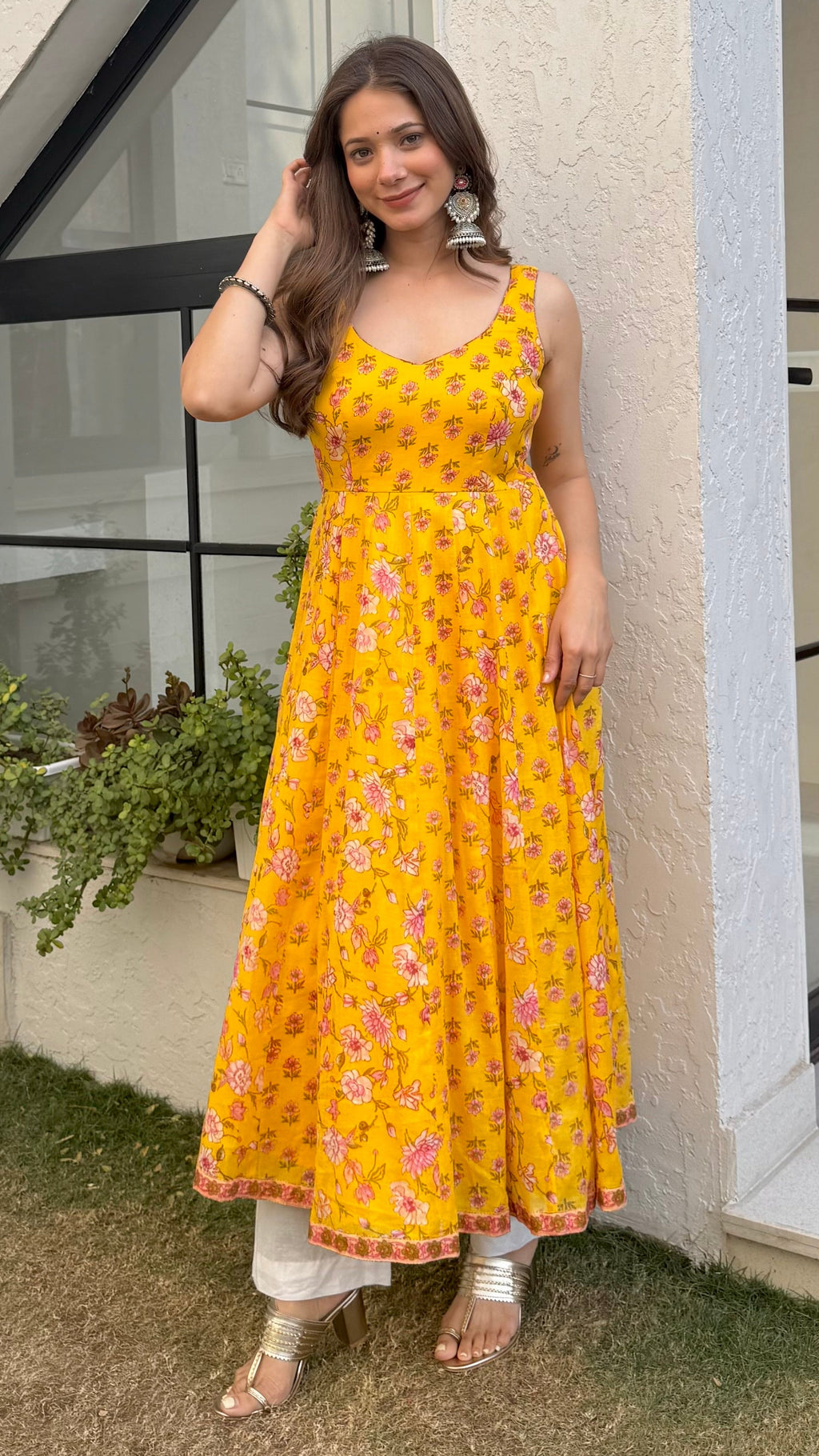 Woman in a yellow floral dress standing outside a modern house.